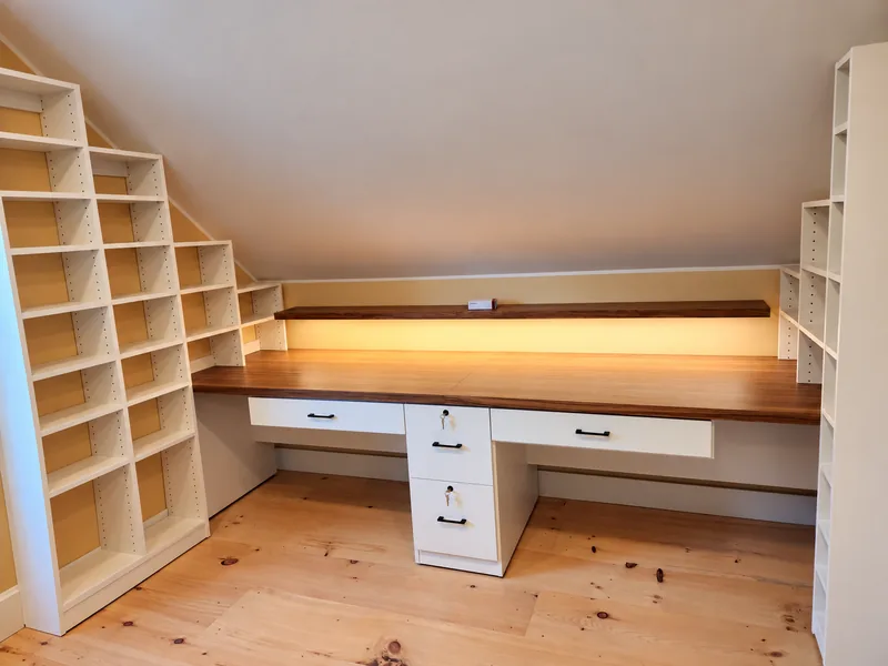 Built-in attic desk with a wood countertop, four drawers, open shelves and warm integrated lighting
