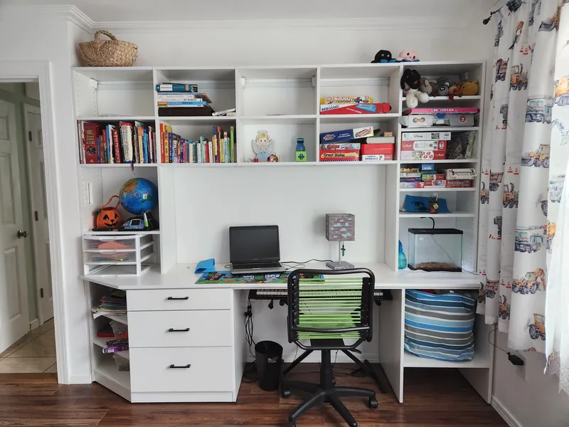 White built-in study with a desk, drawers, book shelves and a green desk chair