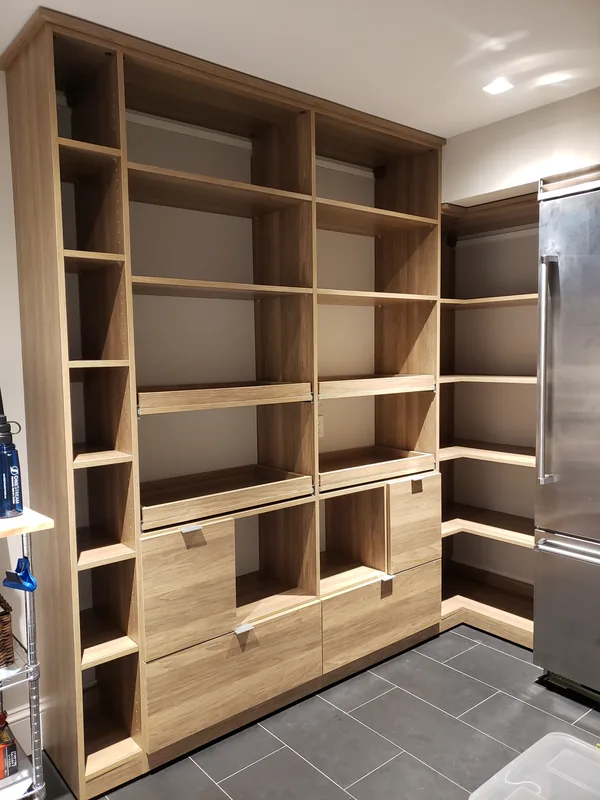 Wood-finish pantry with adjustable shelves, pull-out trays and lower storage beside a refrigerator