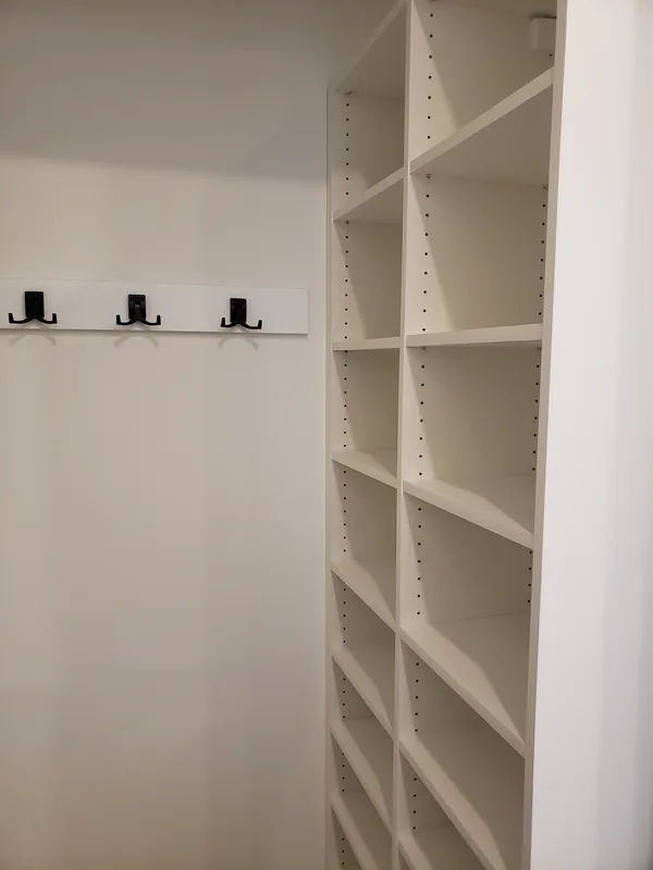White entry closet with black coat hooks and adjustable side shelving