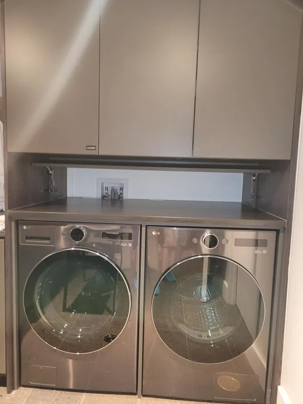 Taupe laundry cabinetry with three upper doors, an open recess and a countertop above a washer and dryer