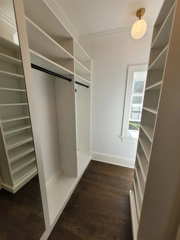 White walk-in closet with tall adjustable shelves, hanging rails and dark wood flooring