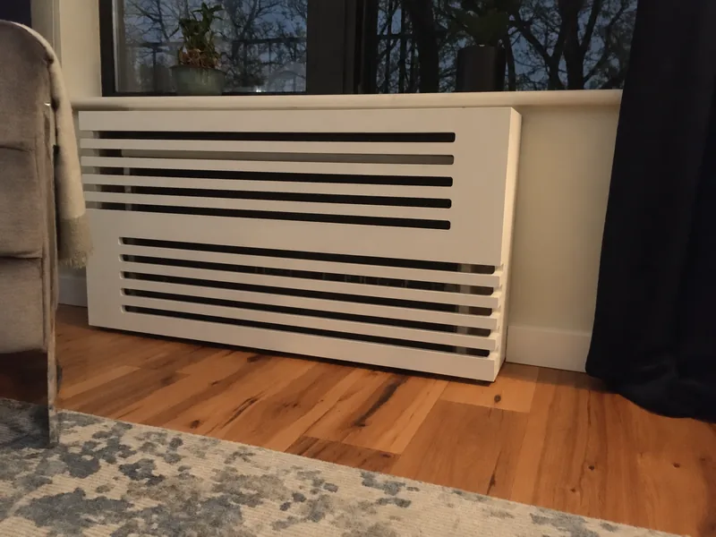 White radiator cover with horizontal ventilation slats beneath a window