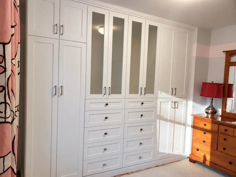 White bedroom wardrobe with reflective glazed doors, side cupboards and two banks of drawers