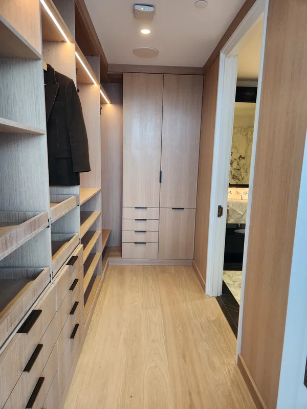 Wood-finish walk-in closet with illuminated shelves, hanging spaces and drawers